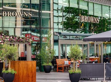 Outdoor seating area of Browns restaurant with greenery and wooden benches.