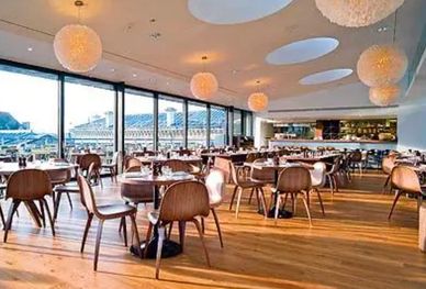 Modern restaurant interior with wooden chairs and large windows.