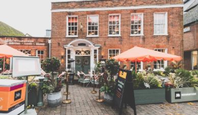 Outdoor seating area of a brick building with orange umbrellas and plants.