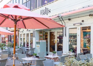 Outdoor seating area of Bill's restaurant with pink umbrellas and tables.