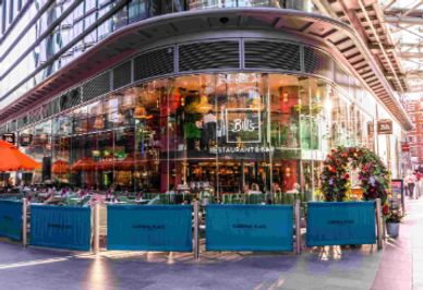 Modern restaurant with outdoor seating and vibrant city reflections.