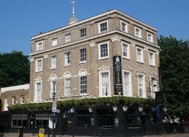 Historic multi-story brick building with a pub on the ground floor under clear blue sky.