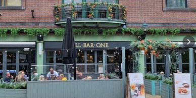 Outdoor seating area of a bar with patrons and greenery decorations.