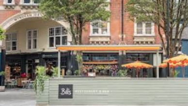 Outdoor seating area of a bar with orange umbrellas in a city setting.