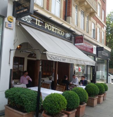 Outdoor seating at Il Portico restaurant with green potted plants.