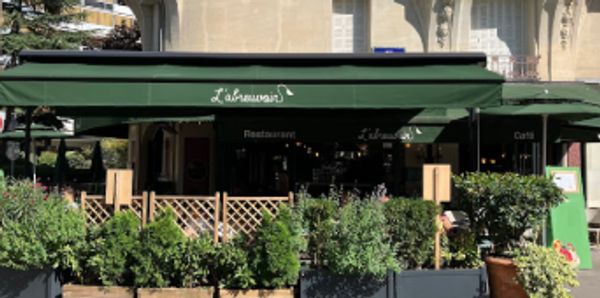 Outdoor view of a green-awning café with lush plants in front.