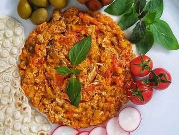 A colorful plate with scrambled eggs, olives, tomatoes, radishes, and herbs.