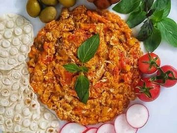 A colorful plate with scrambled eggs, olives, tomatoes, radishes, and herbs.