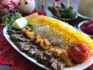 A plate of grilled meat, saffron rice, grilled tomato, and fresh vegetables.