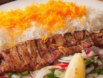 Grilled kebab served with saffron rice, grilled tomato, and fresh salad.