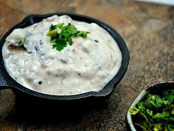 A creamy white sauce garnished with fresh green herbs in a black bowl.