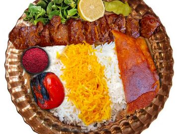 Plate of Persian kebab with rice, grilled tomato, herbs, and lemon.