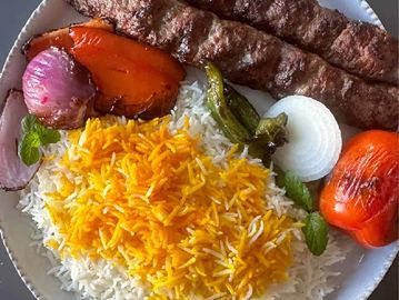 Plate of kebabs with saffron rice, grilled vegetables, and onions.
