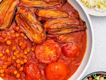 A bowl of spicy tomato stew with chickpeas and eggplants, served with rice and vegetable salad.
