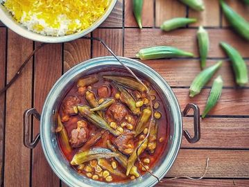 A bowl of okra stew with a side of saffron rice on a wooden table.