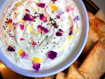 Bowl of creamy dip with rose petals and pita chips on a plate.