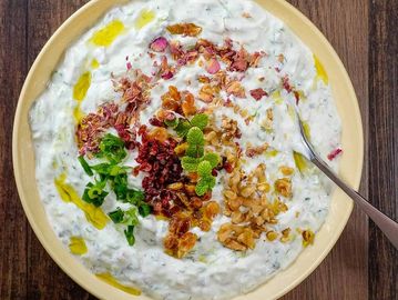Creamy yogurt dip garnished with nuts, herbs, and spices in a beige bowl.