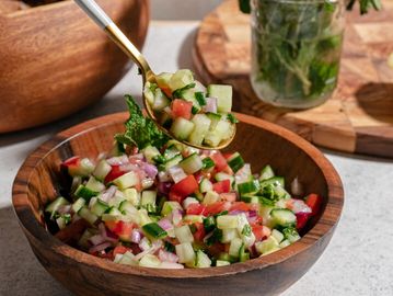 Colorful fresh vegetable salad in a wooden bowl with a gold spoon.