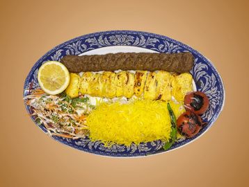 Plate of grilled kebabs with saffron rice, grilled tomatoes, salad, and lemon.