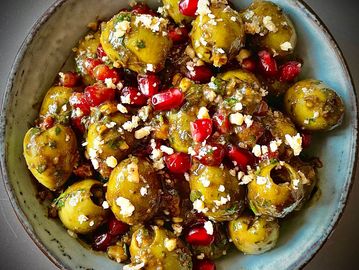 A bowl of seasoned green olives with pomegranate seeds and crumbled nuts.