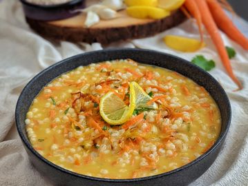 A bowl of savory pearl barley soup garnished with lemon slices and carrots.