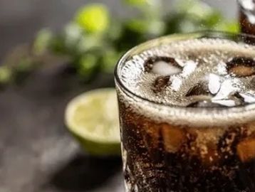 Close-up of a glass of cola with ice cubes and a lime wedge in the background.