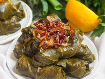 Plate of stuffed grape leaves topped with caramelized onions and served with lemon.