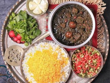 Traditional Persian meal with rice, stew, fresh herbs, and salad on a tray.
