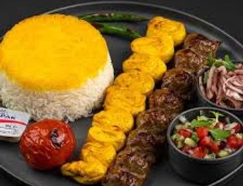 A plate with grilled kebabs, saffron rice, grilled tomato, and fresh salad.
