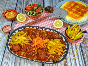 A colorful meal with stew, fries, rice, salad, and lemon halves on a rustic table.