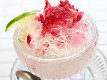 Refreshing pink shaved ice dessert with lime and shredded toppings in a glass bowl.