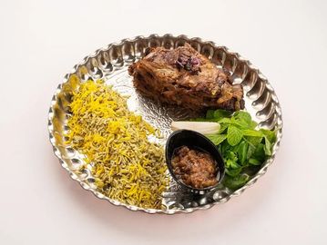 Traditional plate with seasoned rice, spiced meat, fresh herbs, and a side of chutney.
