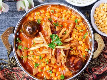 A vibrant chickpea stew garnished with fries and herbs, accompanied by rice and spices.