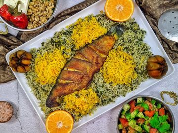 Grilled fish served on a bed of yellow and green rice with oranges and sides.