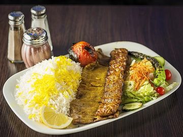 Plate with grilled meat, rice, vegetables, and spices on a wooden table.