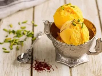 Two scoops of vibrant yellow ice cream in an ornate silver bowl.