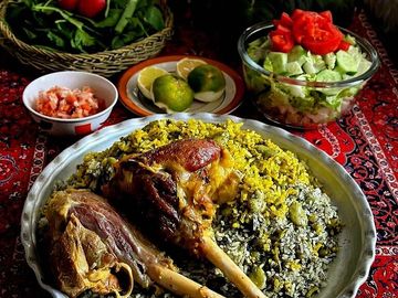 Traditional meal with rice, meat, salad, and fresh vegetables on a patterned tablecloth.
