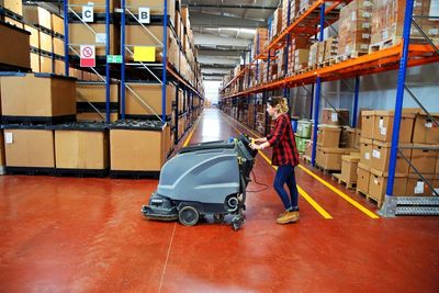 Team member using a walk behind scrubber cleaning the warehouse floor.