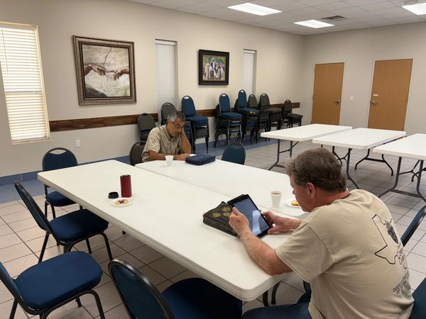 Two men sitting at a white table in a conference room, one using a tablet.