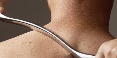 Person using a metal tool to massage or scrape their upper back and neck.