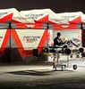 Person working on a go-kart under Precision Works Racing tents at night.