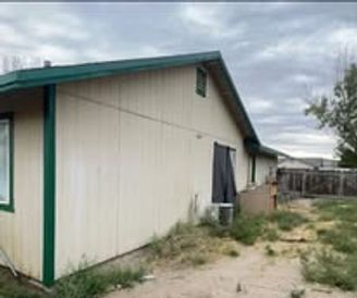 Creme-colored house with green trim, a small dirt yard, and a fence under a cloudy sky