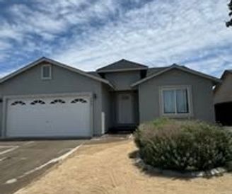 Suburban gray house with a white garage door, sparse landscaping, and a cloudy sky