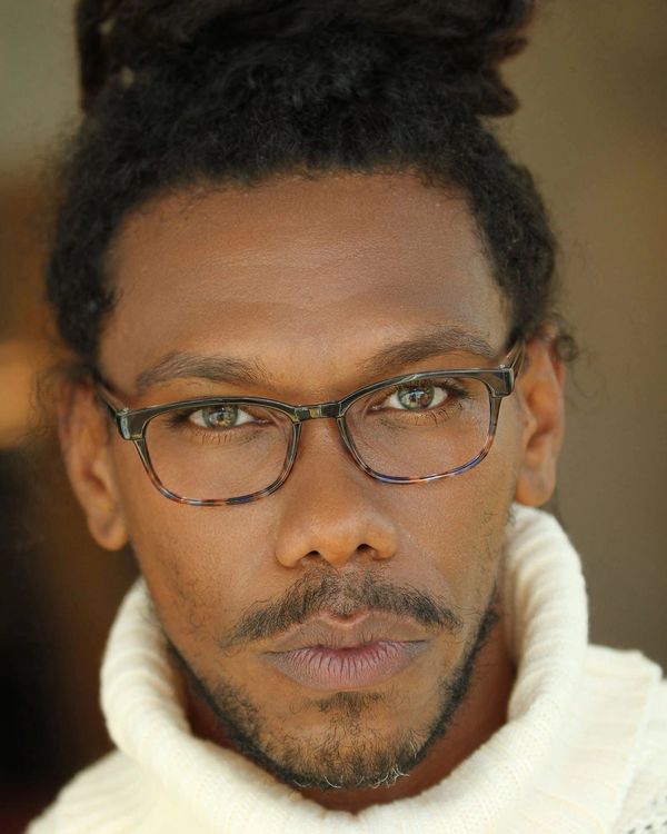 Close-up portrait of a man wearing tortoiseshell glasses and a white turtleneck sweater.