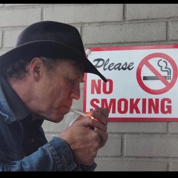 Man lights cigarette near a 'No Smoking' sign.