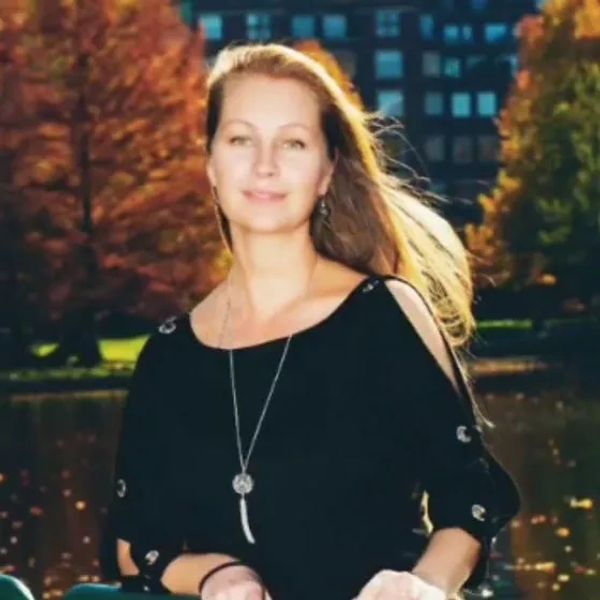Woman in black top standing outdoors with autumn backdrop.