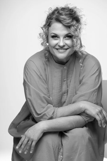 Smiling woman in a coral dress sitting with crossed arms.