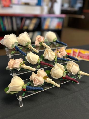 Boutonnieres with white and light pink roses arranged on a clear acrylic stand.