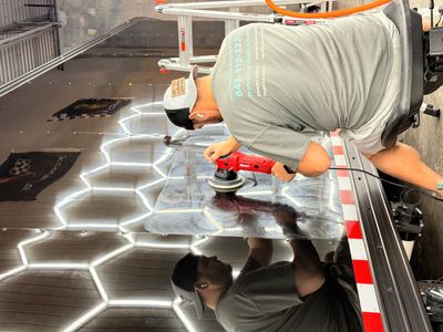 A man polishes a shiny black surface with a power tool indoors.
