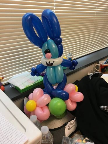 Blue twisted balloon rabbit on a base of pink flowers. Balloon delivery.